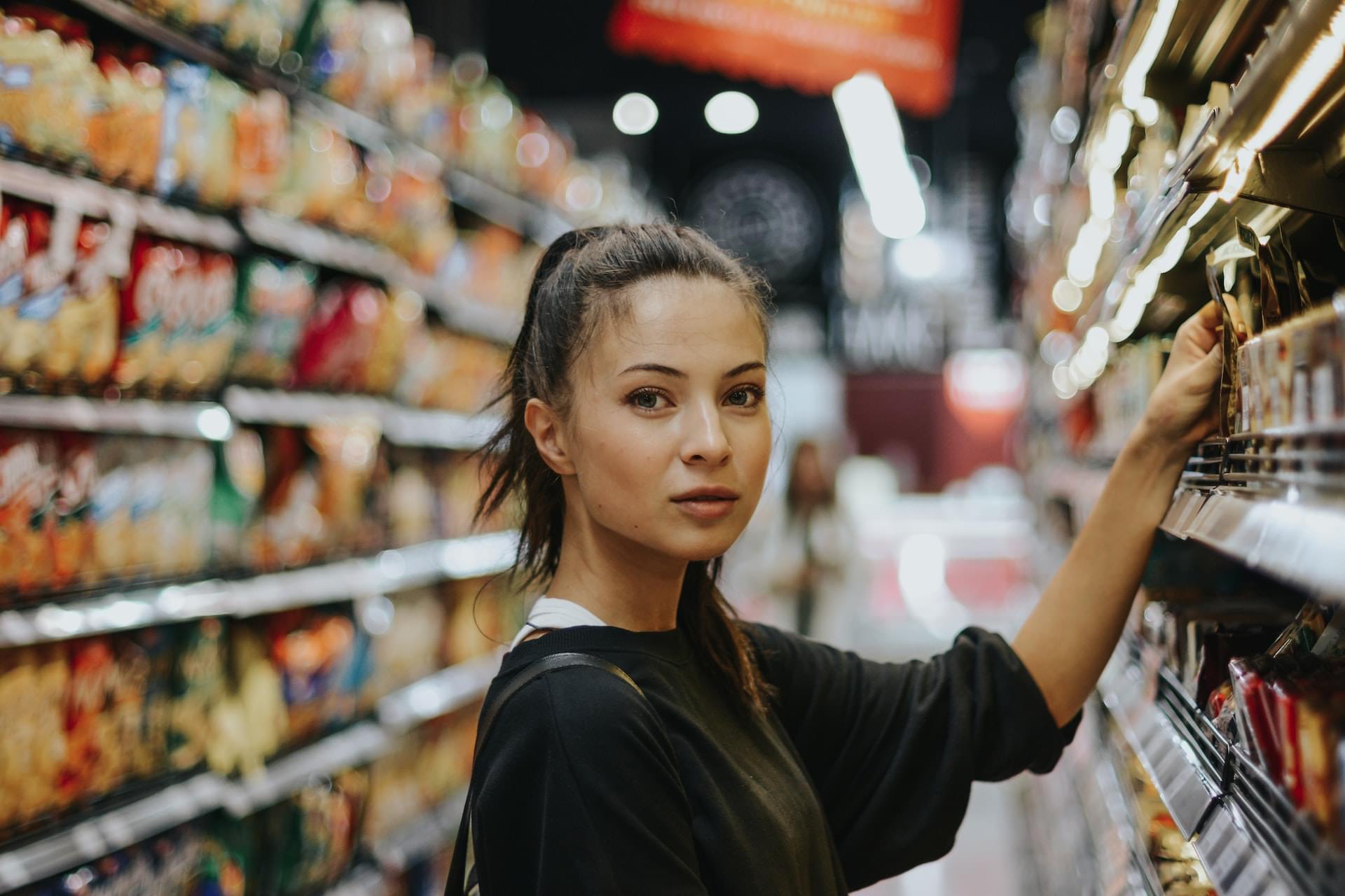 Woman stands in front of supermarket shelf and looks into camera